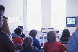 Photograph of the back view of a group of people watching a television screen