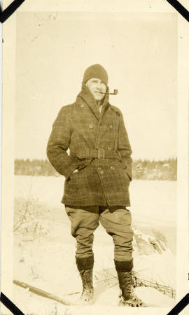 Photograph of Thomas Head Raddall in the snow beside a frozen lake and smoking a pipe