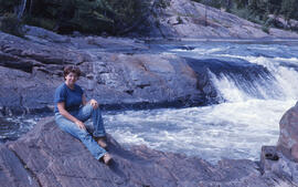 Photograph of Lynne Brennan sitting on the shore of the Wanapitei River, near Sudbury, Ontario