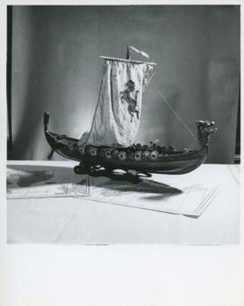 Photograph of a model Viking ship set atop two maps taken in Thomas Head Raddall's study