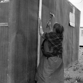 Photograph of Alicie Berthé hammering a nail into her house in Fort Chimo, Quebec