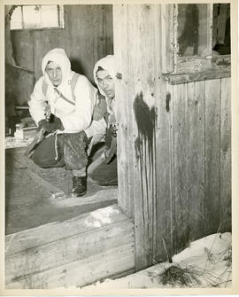 Photograph of two unidentified soldiers sheltering in a small cabin during winter infantry traini...