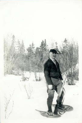 Photograph of Thomas Head Raddall rabbit hunting in the snow, wearing snowshoes and carrying a rifle