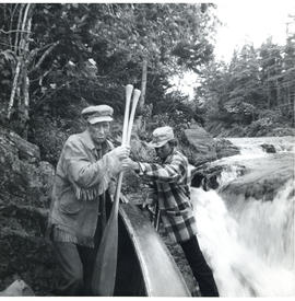 Photograph of a scene with the two actors carrying a canoe and oars near the Sheet Harbour river