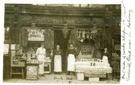 Photograph of four men, including T.H. Raddall, Sr., wearing aprons and standing outside a grocer...