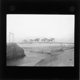 Photograph of people on horseback crossing a bridge