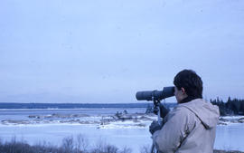 Photograph of a woman looking over a frozen lake with a telescope