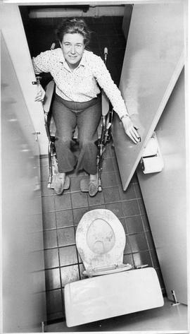 Photograph of Barbara Hinds sitting in a wheelchair in a bathroom stall