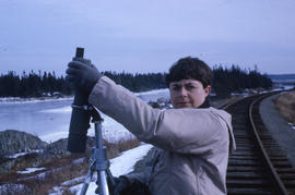 Photograph of a woman standing on train tracks with a telescope