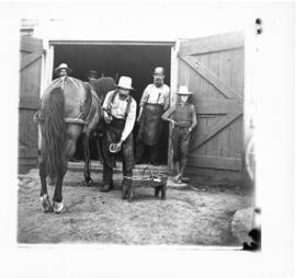 Photograph of men in the doorway of the forge at Milton watching a farrier shoe a horse