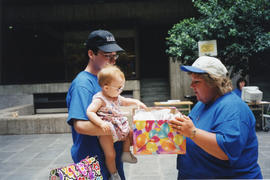Photograph of Audrey LaPierre assisting a man and small child with a prize drawing at the Killam ...