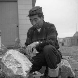 Photograph of Thomasee working with stone and a hatchet in Povungnituk, Quebec