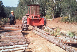 Photograph of an unidentified person standing next to a tractor pulling felled trees in the Irvin...