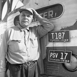 Photograph of an unidentified man standing by a bus near Dawson City, Yukon