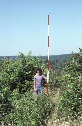 Photograph of an unidentified researcher conducting forest biomass measurements on a bluff in Plo...