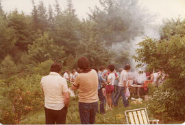 Photograph of a group of unidentified attendees gathered around a barbecue of the First Roscoe Fi...