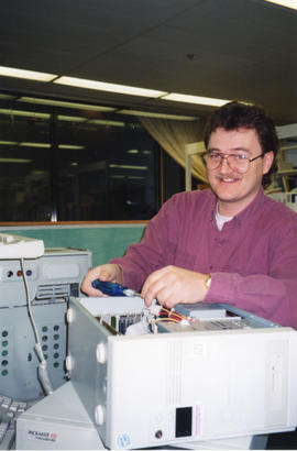 Photograph of David Mifflen fixing a computer in the Information Technology Services Department o...