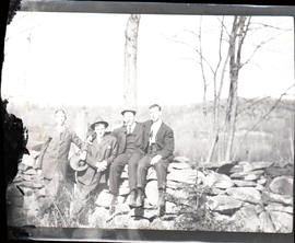 Four men sitting on a rock wall