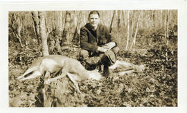 Photograph of Thomas Head Raddall holding his hat and rifle and posing beside the deer that he ha...