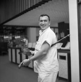 Photograph of an unidentified person with a coffee pot and a walking stick