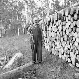 Photograph of Pete Brady standing next to a woodpile with a rifle