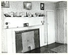 Photograph of the covered fireplace with framed photographs and pieces of art on the mantel and w...