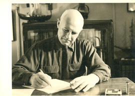 Portrait of Thomas Head Raddall writing at the desk in his study