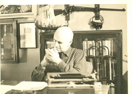 Photograph of Thomas Head Raddall lighting a cigarette while sitting at his desk