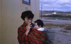 Photograph of a woman holding a baby in a plaid shawl and smoking a cigarette