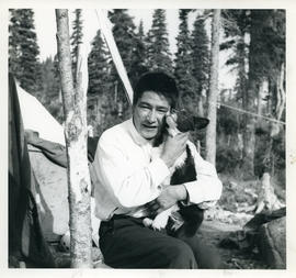 Photograph of a man holding a black and white dog in Davis Inlet, Newfoundland and Labrador