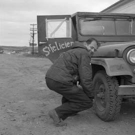 Photograph of Gordon Braley changing the tire of a Jeep in northern Quebec