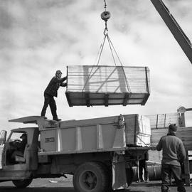 Photograph of a crate being loaded onto a truck with a crane in Fort Chimo, Quebec