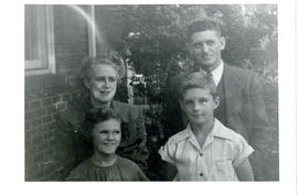 Portrait of Mr. and Mrs. Max Cassidy and their two children standing beside a brick house