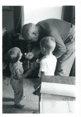 Photograph of Thomas Head Raddall in his study playing with his granddaughter, Deborah, and David...