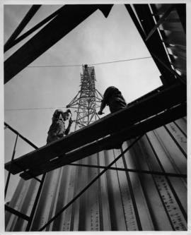Photograph of two people working on an unidentified radio tower