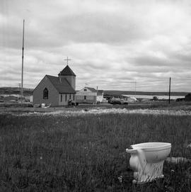 Photograph of a toilet sitting outdoors near a church in Fort Chimo, Quebec