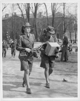 Photograph of two Women's Army Auxiliary Corps women carrying an American flag and a box of loote...