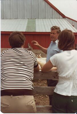 Photograph of three people talking at the side of a sheep pen during the field day at Bill Mathew...